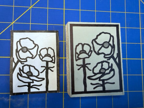 A white piece of paper and a grey block with black Alpine Buttercup images sit on a blue background with yellow lines.