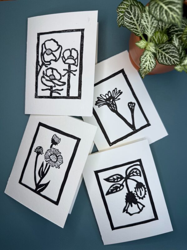 Four black ink wildflower cards on white paper on a green background with a plant