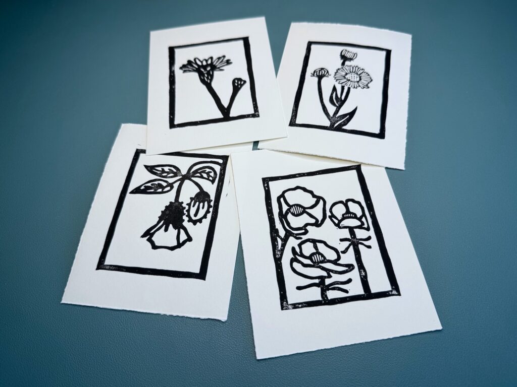 Four black ink wildflower prints on white paper on a green background.