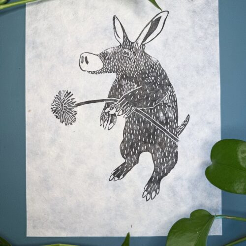 A black ink Aardvark on natural Lokta paper on a green background with a plant