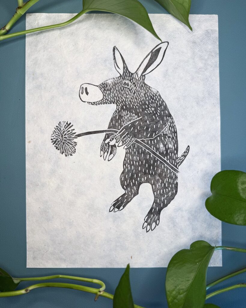 A black ink Aardvark on natural Lokta paper on a green background with a plant