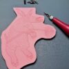 Aardvark progress 2 A red carving tool sits beside a partially carved pink printing block with an Aardvark shape.