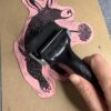 A hand rolls ink with a small brayer onto a pink Aardvark carved block.