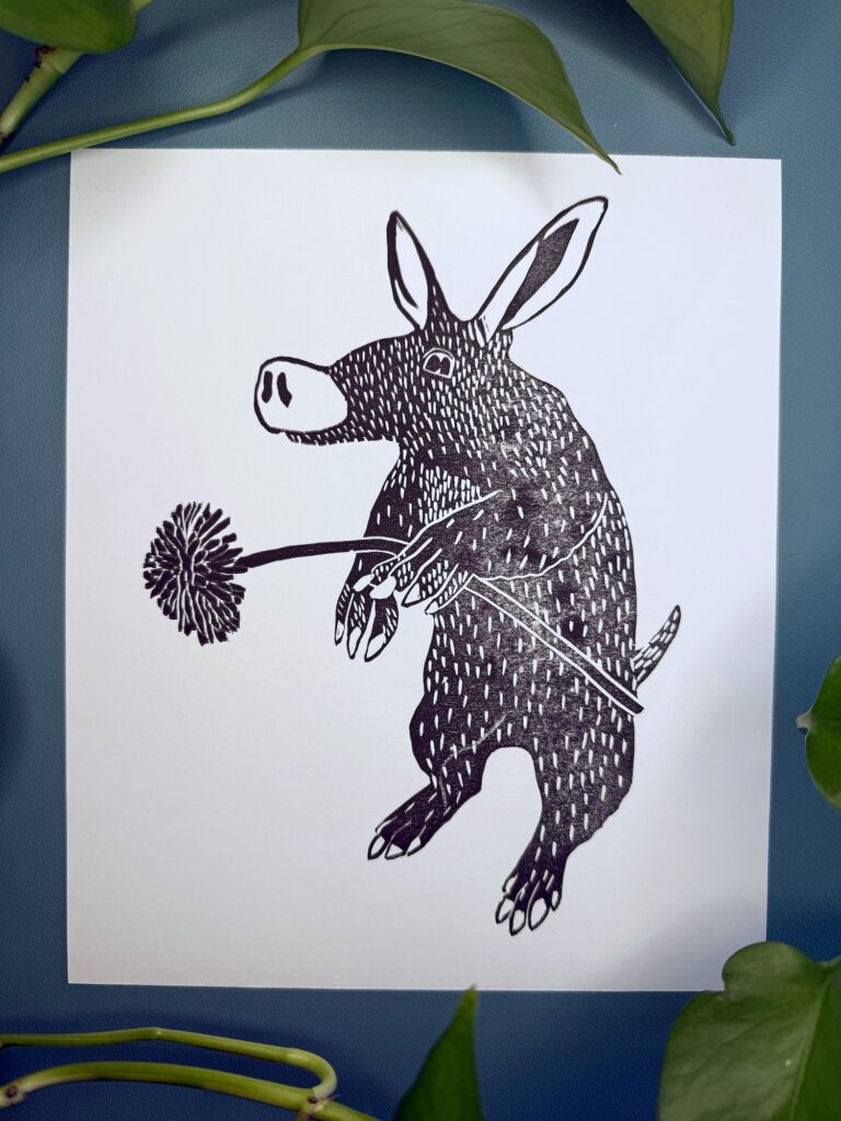 A black ink Aardvark on white paper on a green background with a plant