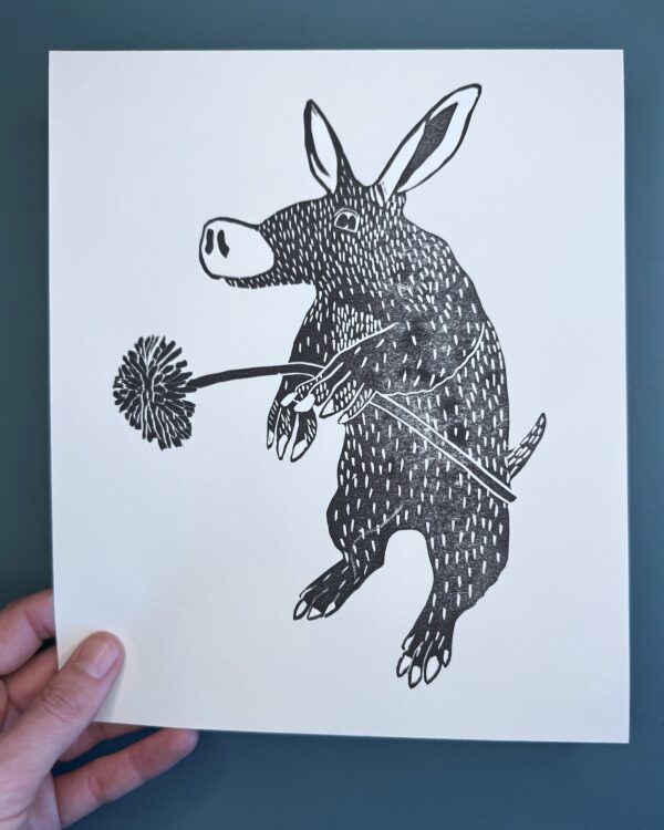 A black ink print of an Aardvark on a white card held over a green background.
