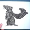 A badger print on white paper held by a hand over a green background