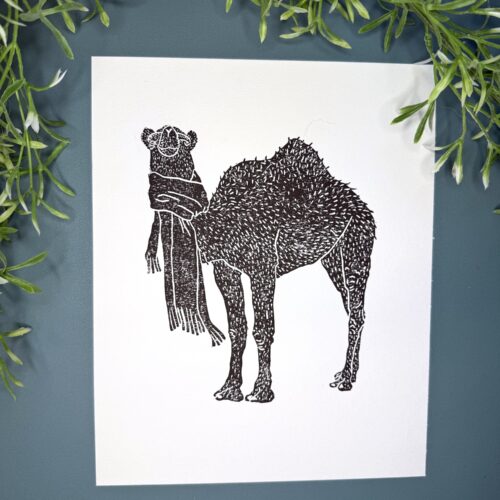 A black ink Camel print on white paper on a green background with a plant